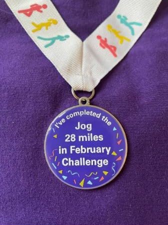 Photo of the medal incentive which features a circular purple medal with the words I've completed the Jog 28 Miles in February Challenge on the front with a party streamer design