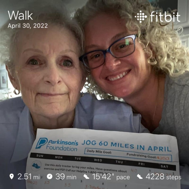 Close up photo of one older woman and one middle-aged woman holding up a Parkinson's Foundation Challenge distance tracker. The photo has information from Fitbit overlayed with a details from a Walk completed on April 30, 2022.